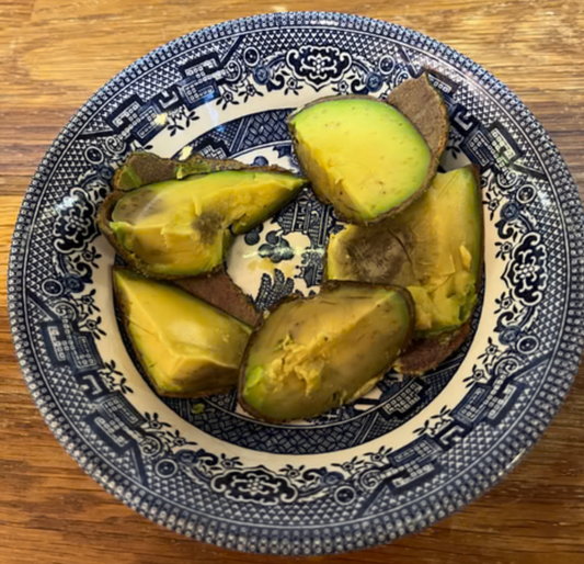 A patterned ceramic bowl containing pieces of ripe, bruised avocado on a wooden surface, ready to be used for a homemade avocado face mask.