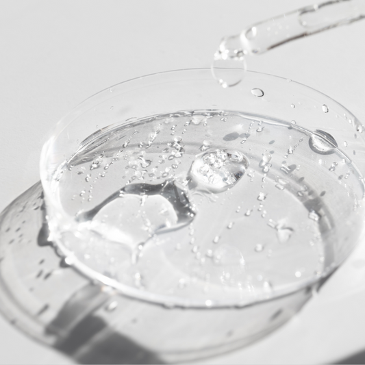 Clear hyaluronic acid serum with bubbles in a glass petri dish, shown with a dropper against a light background.