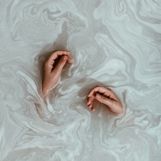 Two hands resting in a creamy, milky bath, showing the soothing and hydrating effect of an oat and chamomile bath soak.
