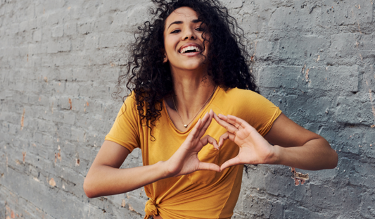 Woman in yellow shirt holding hands in heart shape over her heart