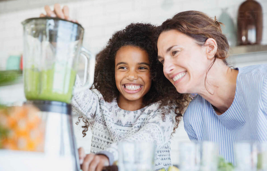 Smiling, enthusiastic mother and daughter making healthy green smoothie in blender in kitchen