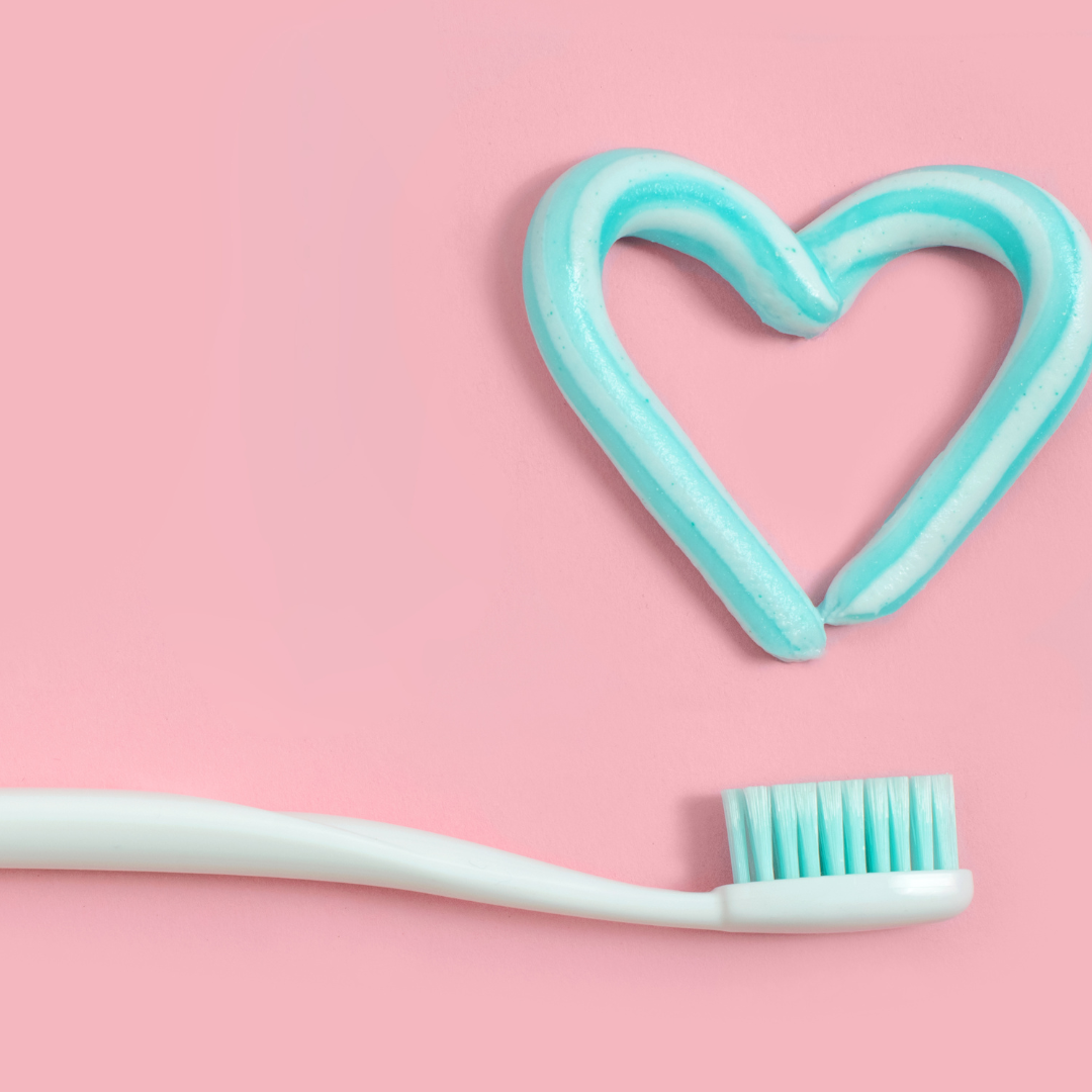 toothpaste on a pink back ground, in the shape of a heart, a white toothbrush is placed below the heart made from toothpaste 
